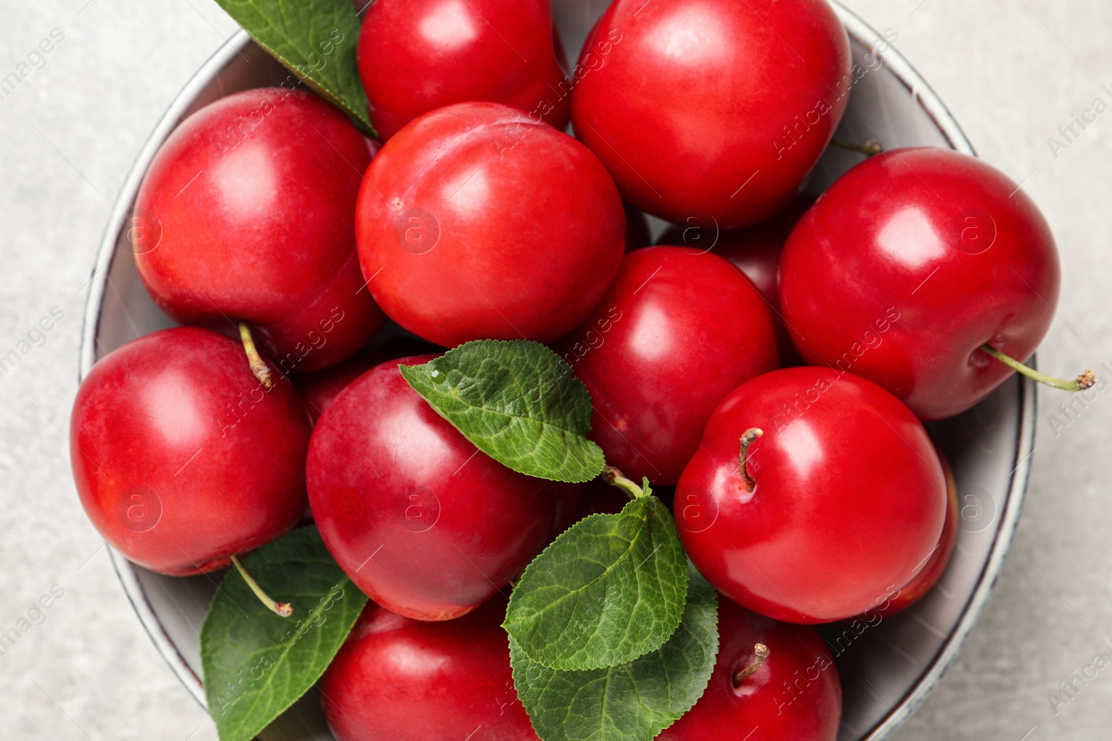 Photo of Delicious ripe cherry plums with leaves on light table, top view