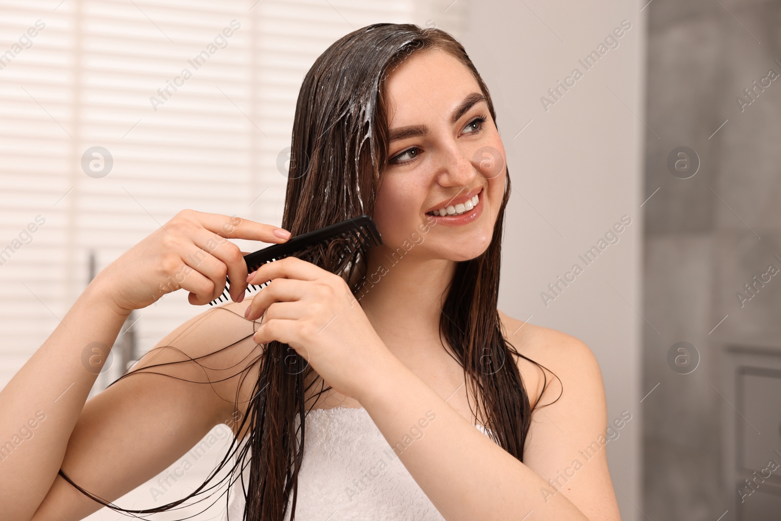 Photo of Young woman brushing hair after applying mask in bathroom