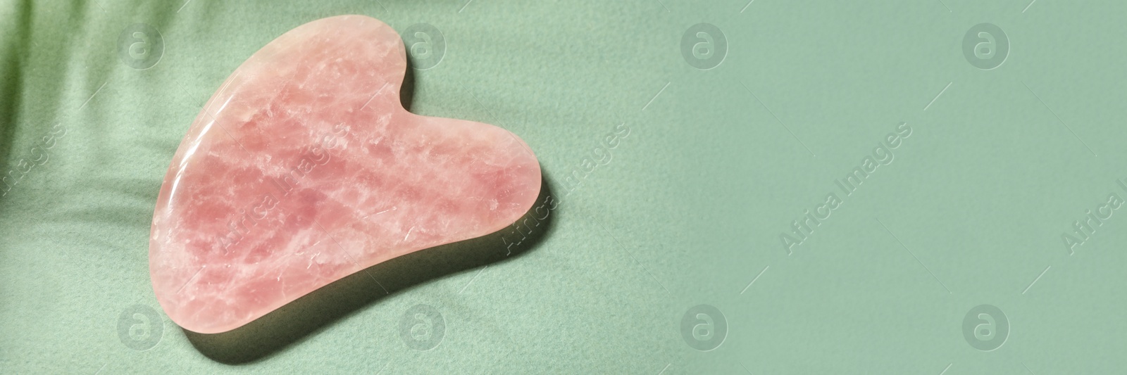 Image of Rose quartz gua sha tool on green background, top view with space for text. Banner design