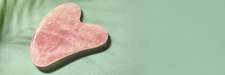 Rose quartz gua sha tool on green background, top view with space for text. Banner design