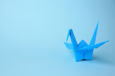 Photo of Origami art. Handmade paper crane on light blue background, space for text