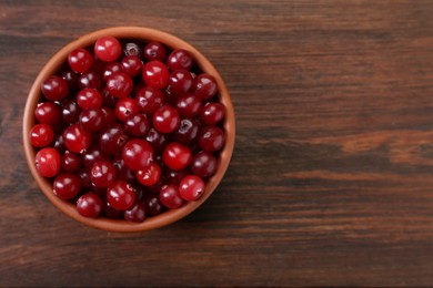 Photo of Fresh ripe cranberries in bowl on wooden table, top view. Space for text