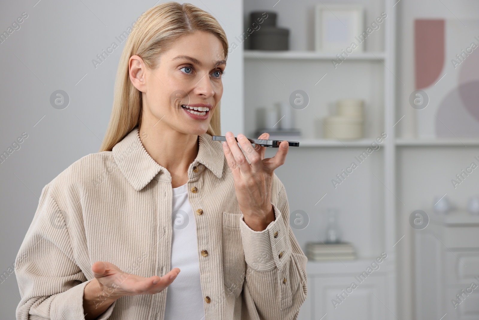 Photo of Woman recording voice message via smartphone at home, space for text