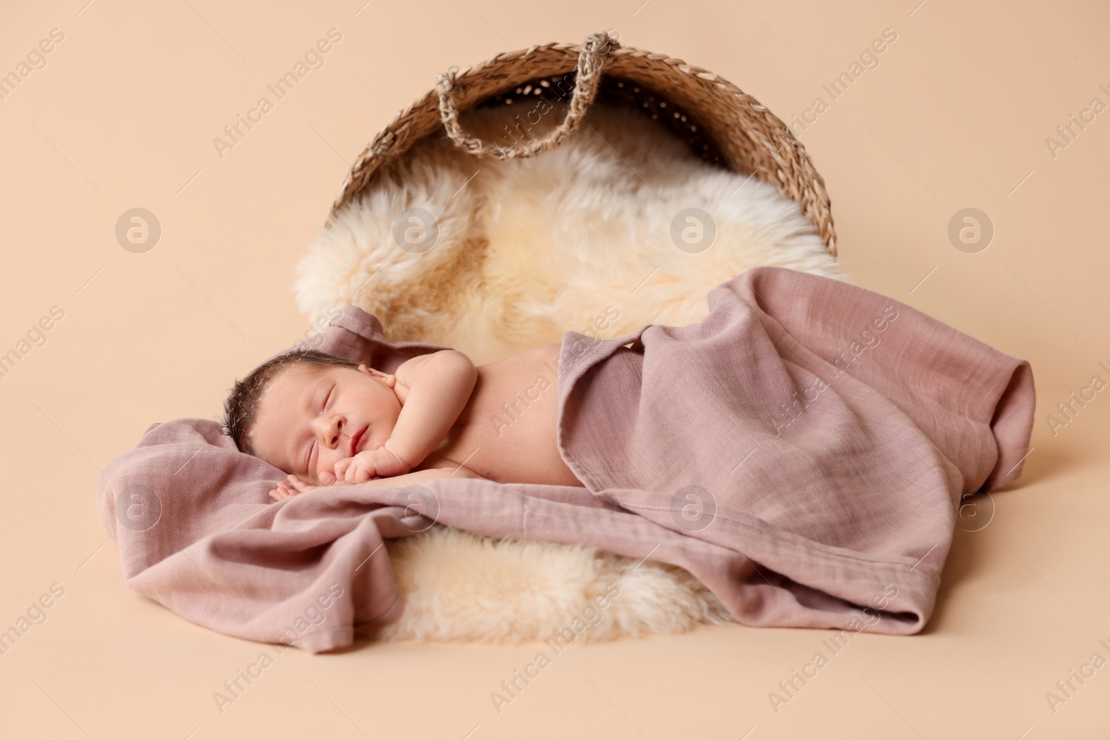 Photo of Adorable newborn baby sleeping on faux fur near overturned wicker basket against beige background