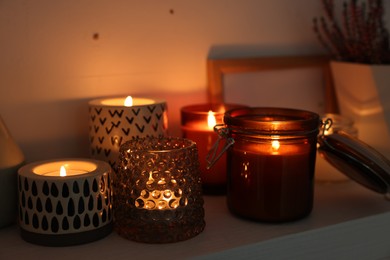 Beautiful burning wax candles on white shelf