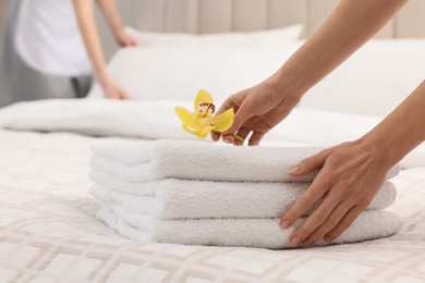 Photo of Chambermaid putting flower on fresh towels in hotel bedroom, closeup