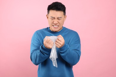 Emotional asian man with bubble wrap on pink background