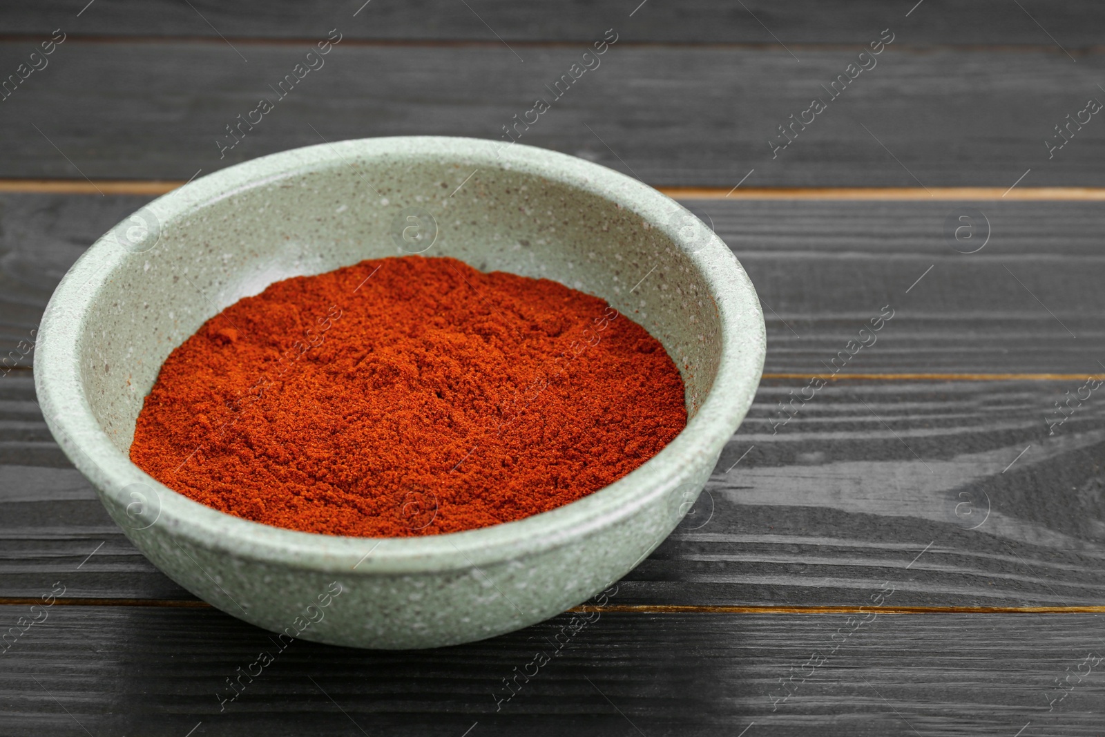 Photo of Bowl of aromatic paprika on black wooden table. Space for text