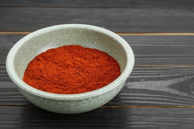 Bowl of aromatic paprika on black wooden table. Space for text