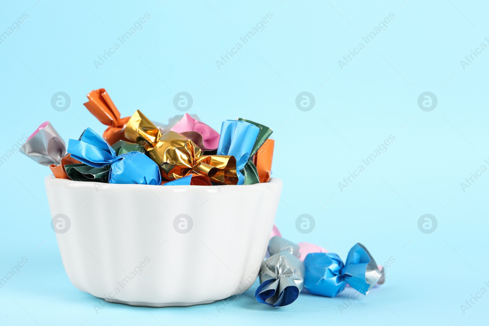 Photo of Candies in colorful wrappers on light blue background, space for text