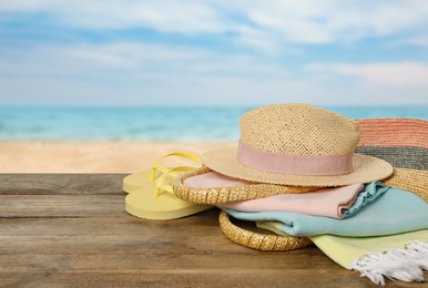 Beach bag with towel, hat and flip flops on wooden surface near seashore. Space for text