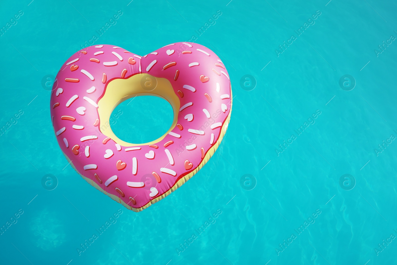 Photo of Heart shaped inflatable ring floating in swimming pool on sunny day, above view. Space for text