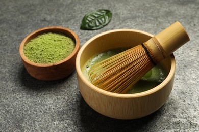 Photo of Cup of fresh matcha tea with bamboo whisk and green powder on grey table, closeup