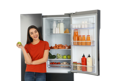 Young woman with apple near open refrigerator on white background