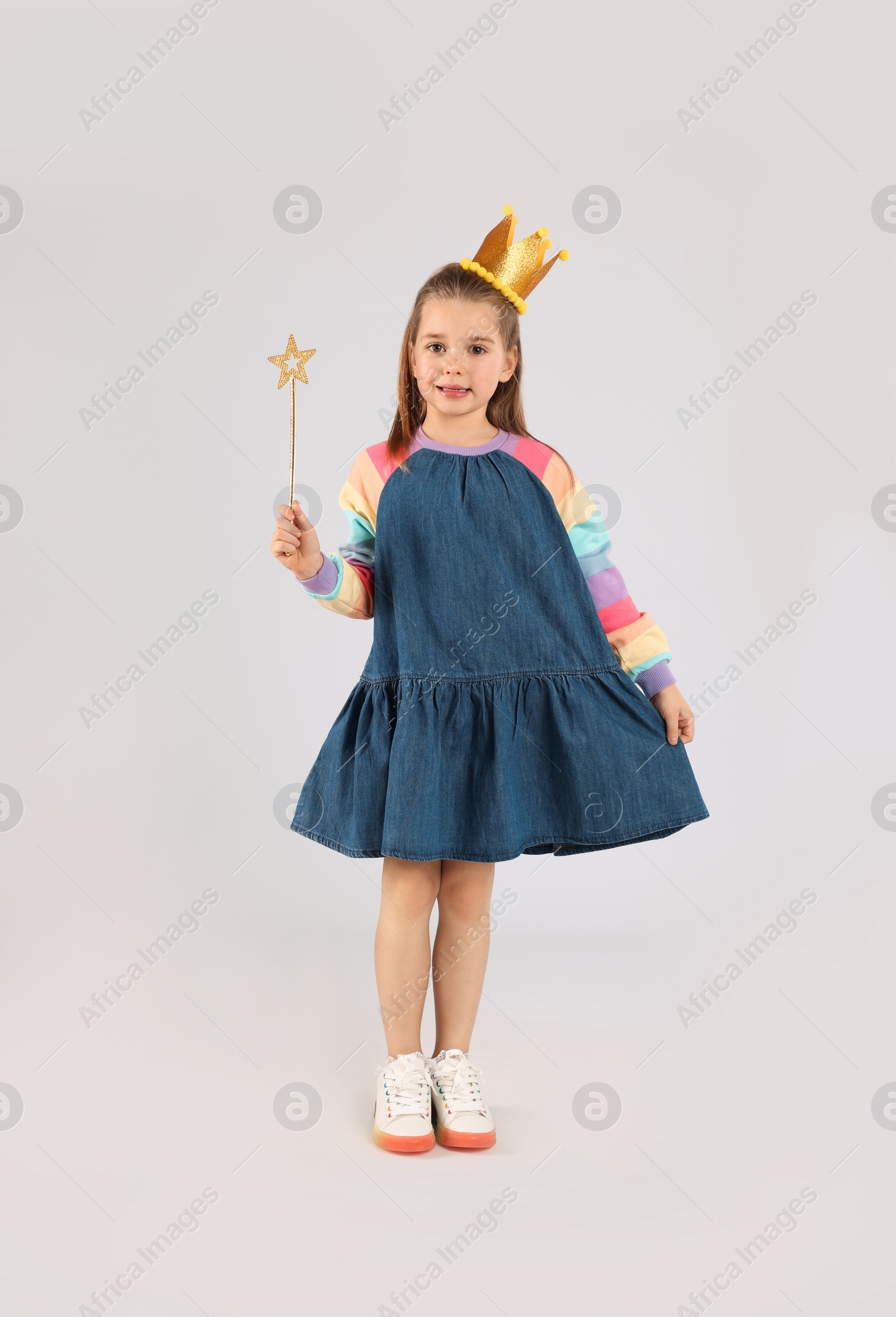 Photo of Cute girl in golden crown with magic wand on light grey background. Little princess