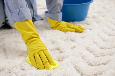 Photo of Woman in rubber gloves cleaning carpet with rag, closeup. Space for text