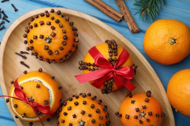 Pomander balls made of tangerines with cloves and fir branch on light blue wooden table, flat lay