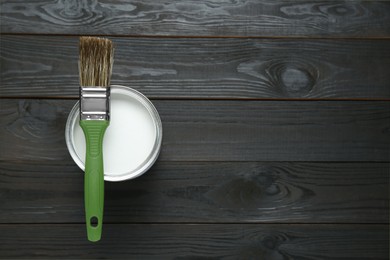 Photo of Can of white paint with brush on black wooden table, top view. Space for text