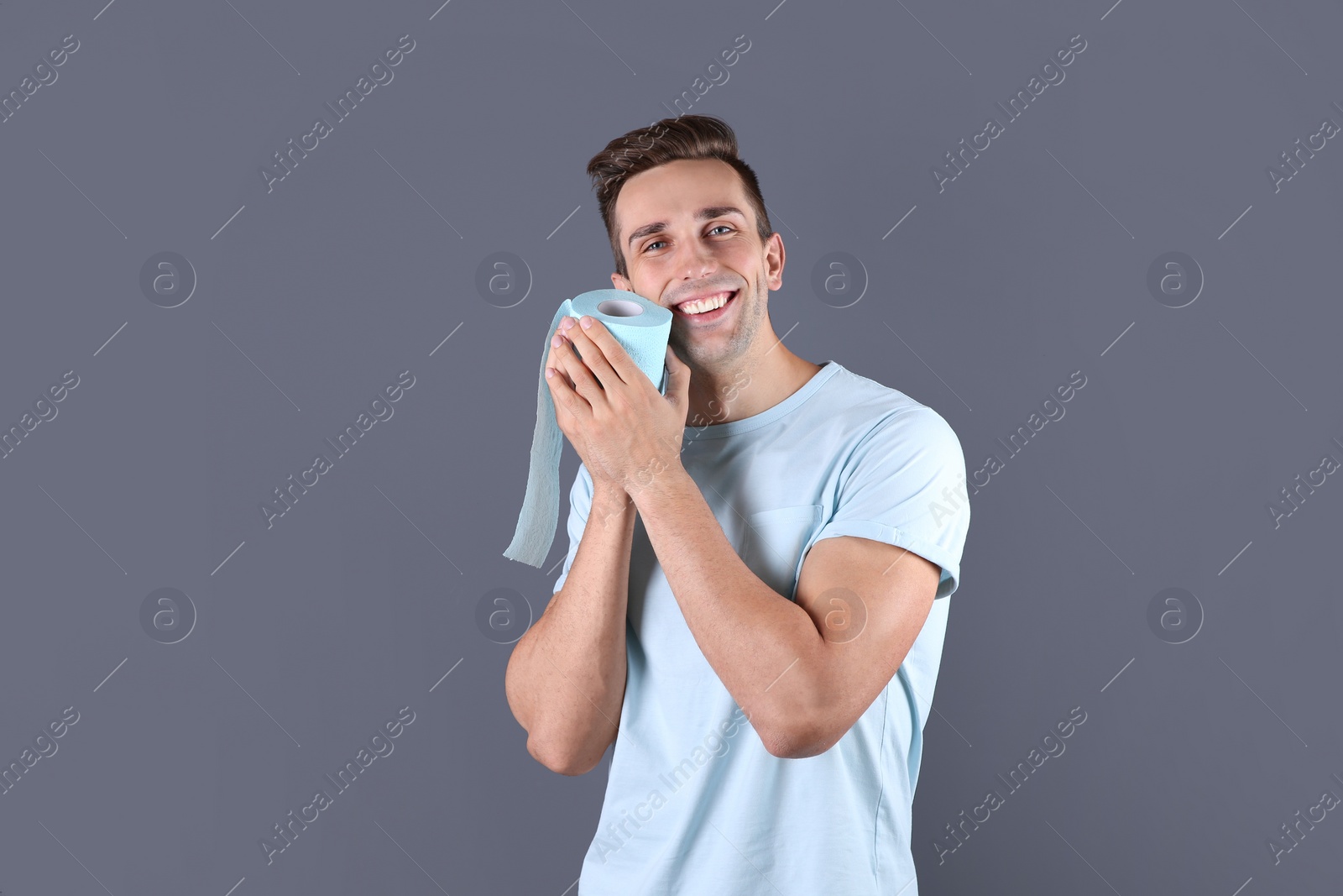 Photo of Young man holding toilet paper roll on color background