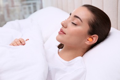 Photo of Young woman with foam ear plugs sleeping in bed