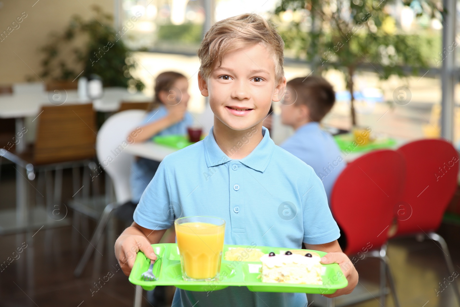 Photo of Cute boy holding tray with healthy food in school canteen