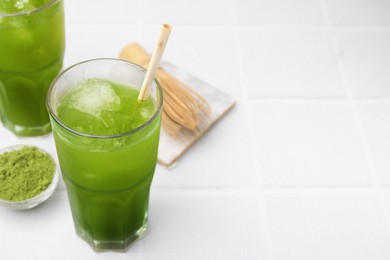 Delicious iced green matcha tea, powder and bamboo whisk on white tiled table, space for text