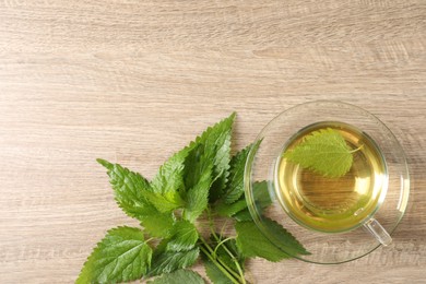 Glass cup of aromatic nettle tea and green leaves on wooden table, flat lay. Space for text