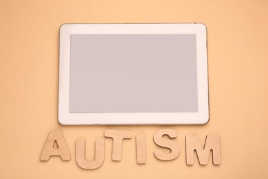 Photo of Word Autism made of wooden letters and tablet on beige background, flat lay