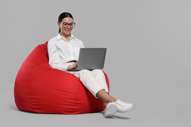 Happy woman with laptop sitting on beanbag chair against light gray background