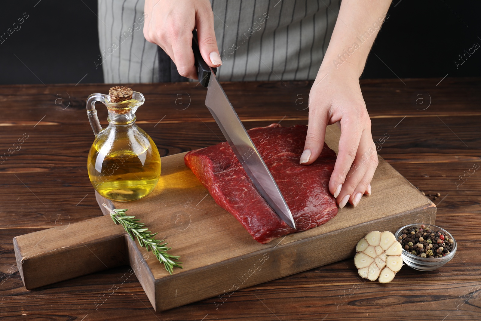 Photo of Woman cutting fresh raw beef steak at wooden table, closeup