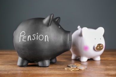 Photo of Black piggy bank with word "PENSION", white one and coins on wooden table