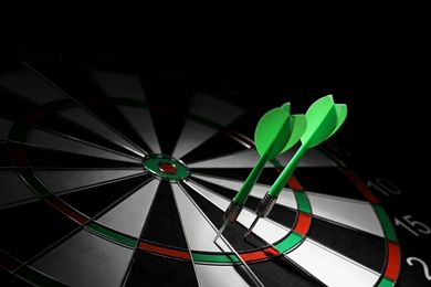 Photo of Green arrows hitting dart board against black background. Space for text