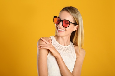 Beautiful woman in stylish sunglasses on yellow background