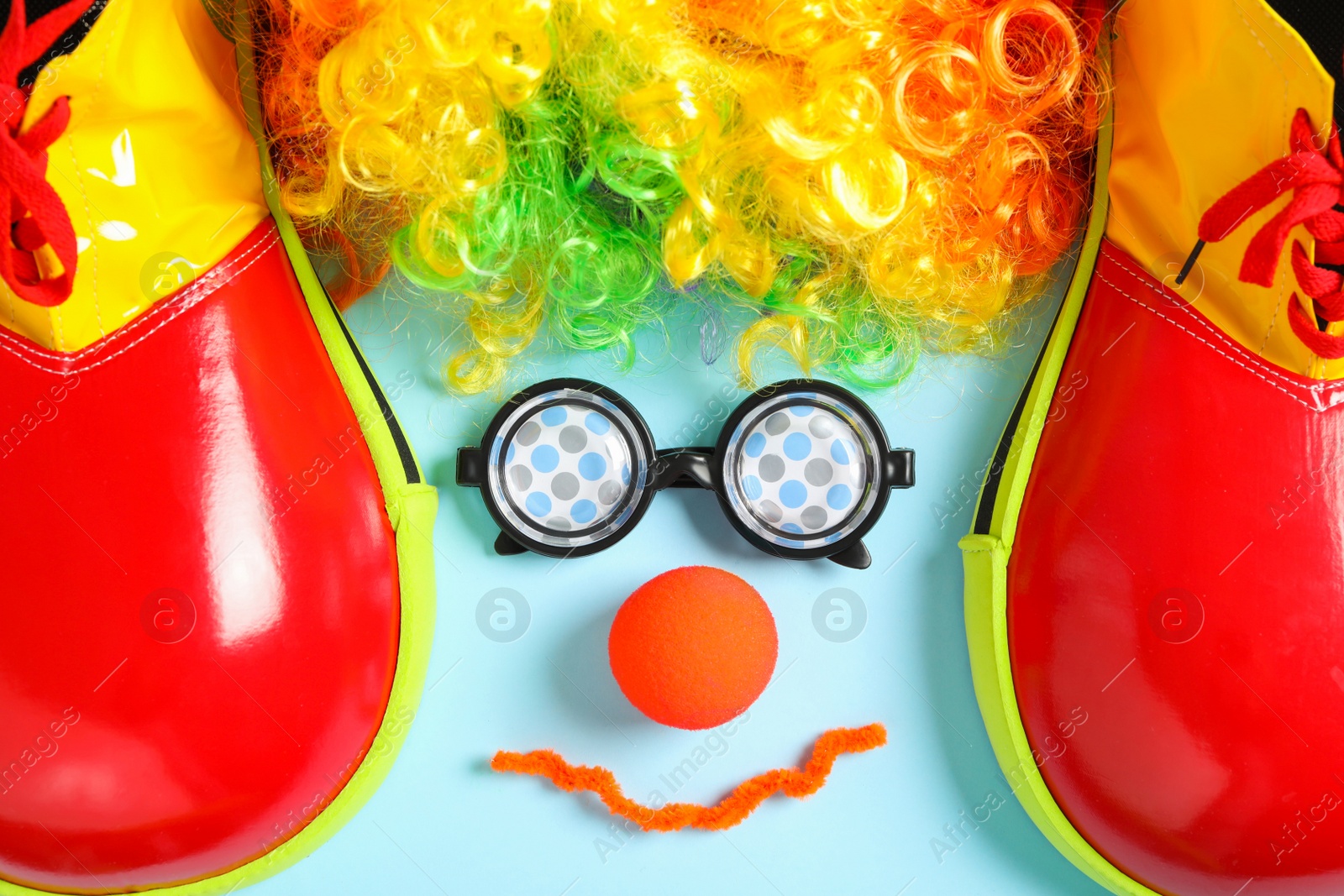 Photo of Funny face made with clown's accessories on light blue background, flat lay