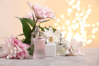 Photo of Bouquet of beautiful lily flowers and perfume bottles on table against beige background with blurred lights, closeup