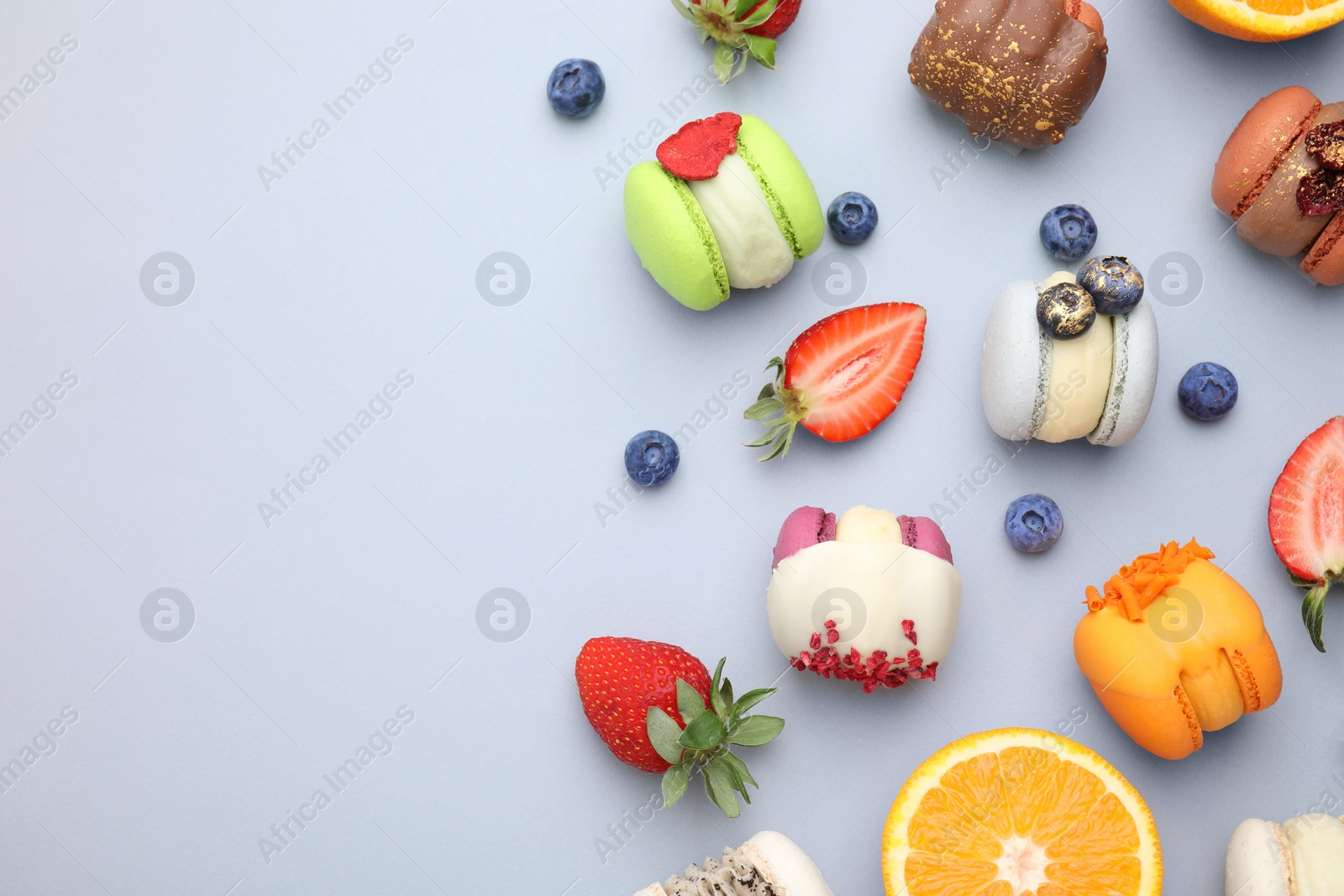 Photo of Delicious macarons, orange and berries on light blue table, flat lay. Space for text