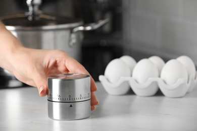 Photo of Woman winding up kitchen timer at white table indoors, closeup. Space for text