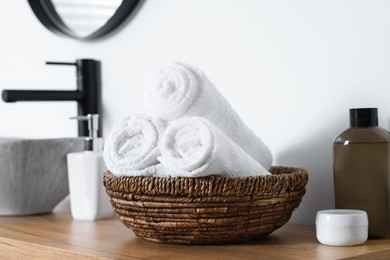 Photo of Wicker bowl with rolled bath towels on wooden table in bathroom