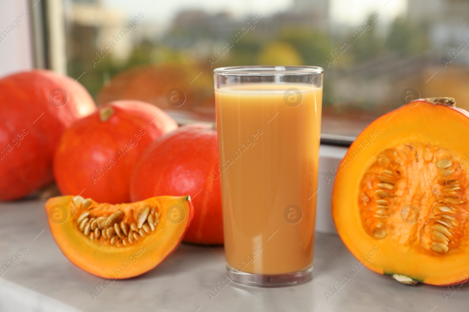 Photo of Tasty pumpkin juice in glass, whole and cut pumpkins on windowsill indoors