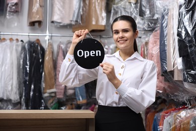 Dry-cleaning service. Happy worker holding Open sign indoors, space for text