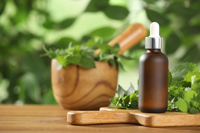 Photo of Glass bottle of nettle oil with dropper and leaves on wooden table against blurred background, space for text