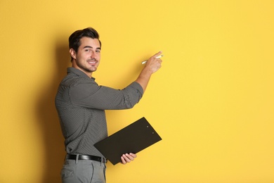 Photo of Young male teacher with clipboard on yellow background. Space for text