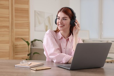 Happy woman with headphones and laptop at wooden table in room