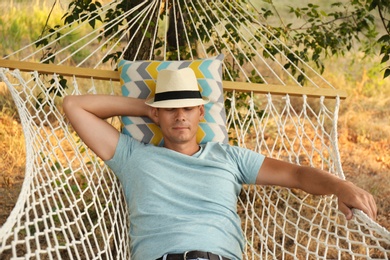 Photo of Man with hat resting in comfortable hammock at green garden