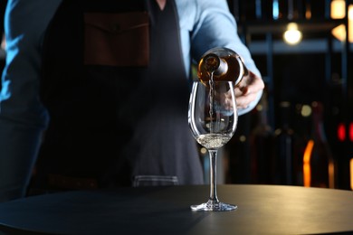 Bartender pouring white wine from bottle into glass at table indoors, closeup. Space for text