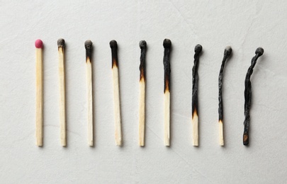 Photo of Row of burnt matches and whole one on light background, flat lay. Human life phases concept