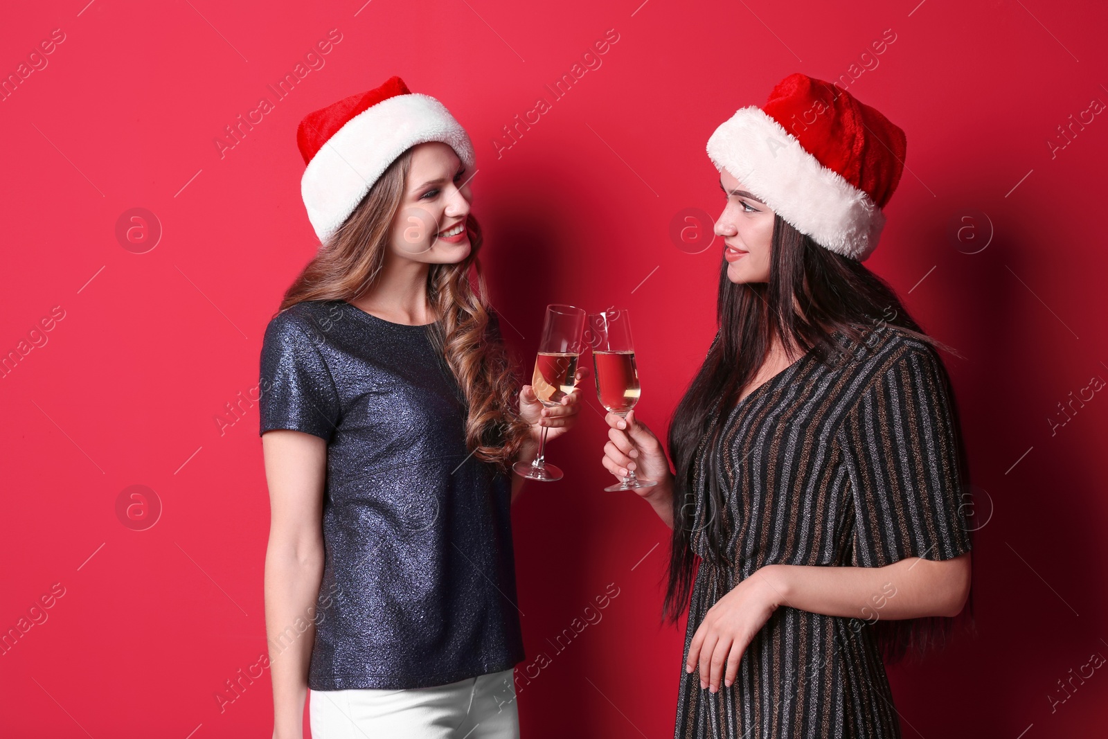 Photo of Beautiful young women in Santa hats with glasses of champagne on color background. Christmas celebration