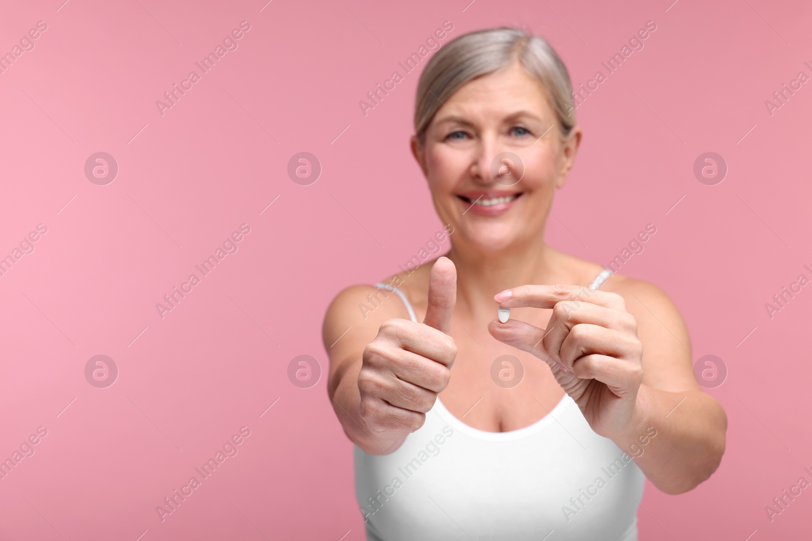 Photo of Beautiful woman with vitamin pill showing thumbs up on pink background, selective focus. Space for text