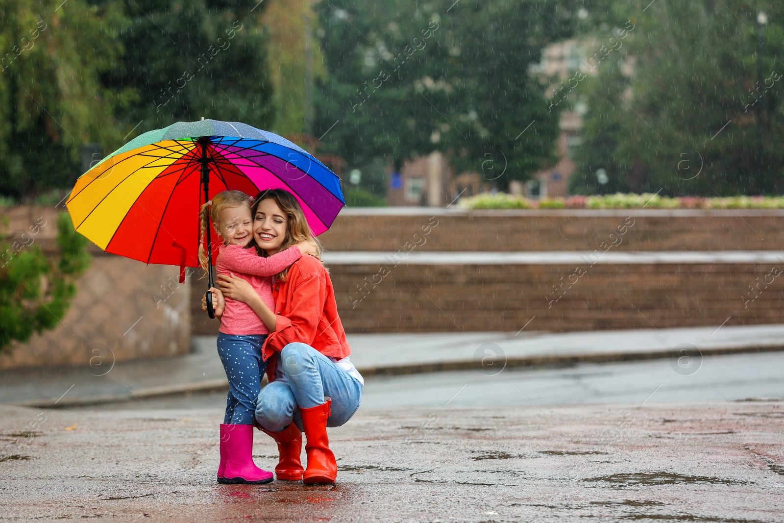 Photo of Happy mother and daughter with bright umbrella under rain outdoors