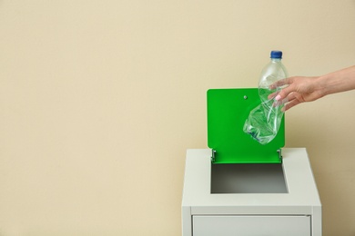 Photo of Woman throwing empty plastic bottle into trash bin on color background, closeup with space for text. Recycling concept